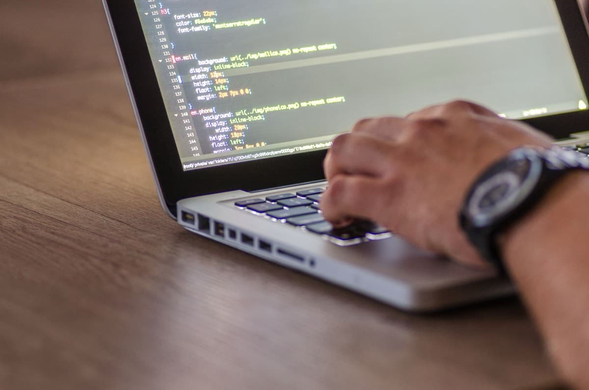 Manos de un técnico trabajando en una laptop con código en pantalla